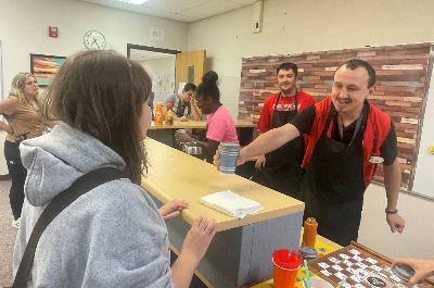  UCNECT student in apron serves coffee cup to student customer